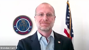 FCC Chair Brendan Carr looks into camera with the FCC seal and flag behind him