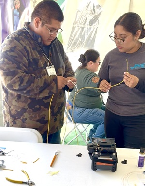 Two young JNET technicians in training work side by side to splice fiber