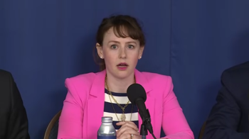 NTIA administrator Arielle Roth seated behind a microphone wearing a pink suit jacket