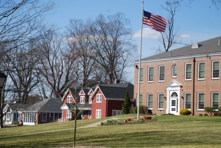 A grassy knoll in Longmeadow MA with Bay Path College brick building in background behind an American flag waving in the breeze
