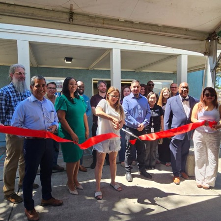 A group of community leaders and housing resident cut red ribbon in front of building
