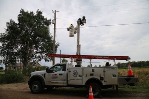 Tri-County Electric Cooperative bucket truck with worker elevated into air checking fiber line on utility pole