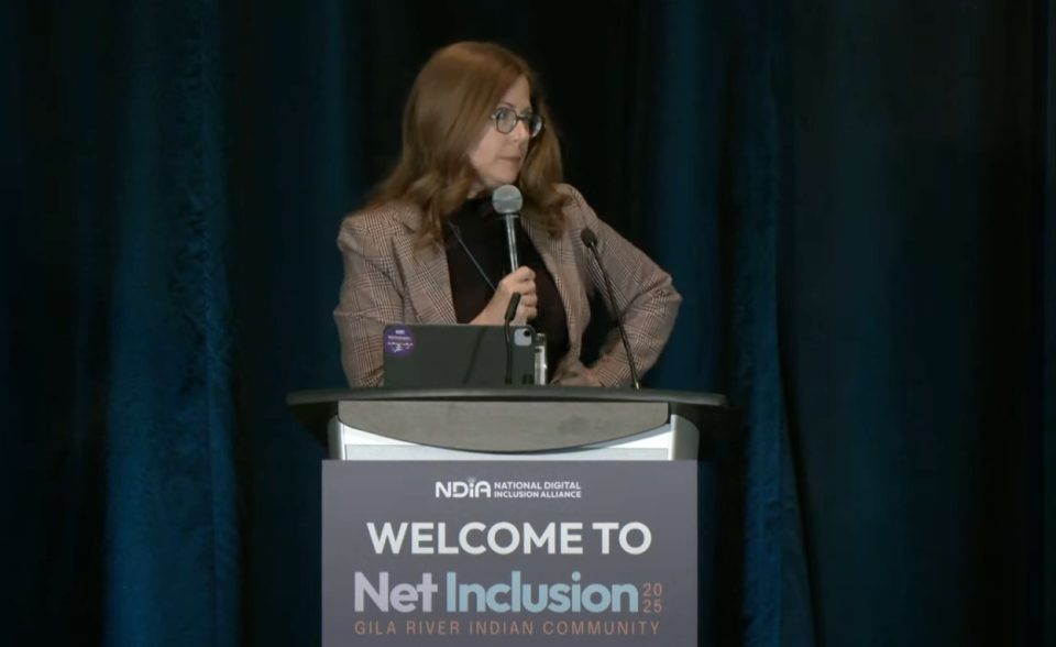 Angela Siefer at Net Inclusion NDIA executive director Angela Siefer holds mic standing behind podium addressing Net Inclusion audience