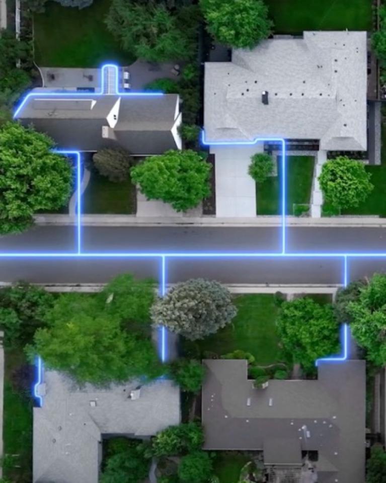 An aerial shot of four residential homes with a blue glowing line connecting each to illustrate the fiber connections