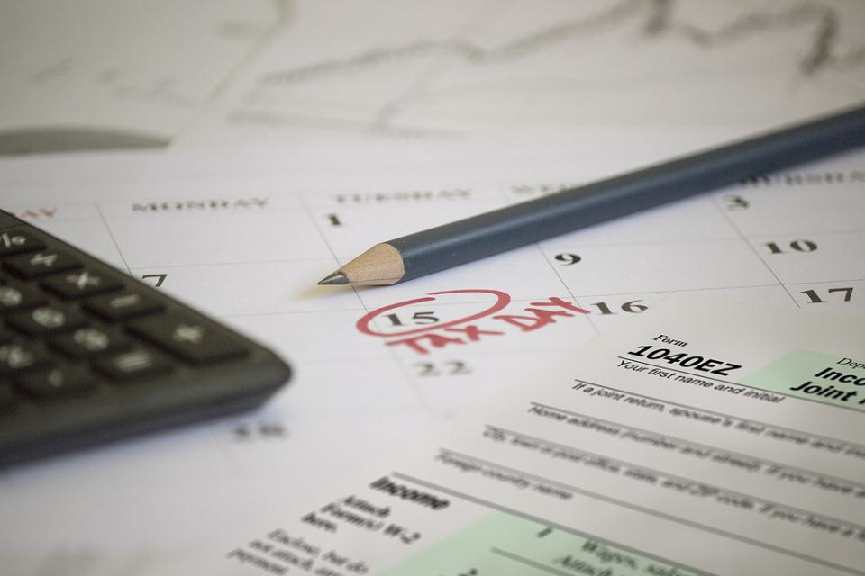 A calculator and tax form lay across a calendar with tax day (April 15) circled