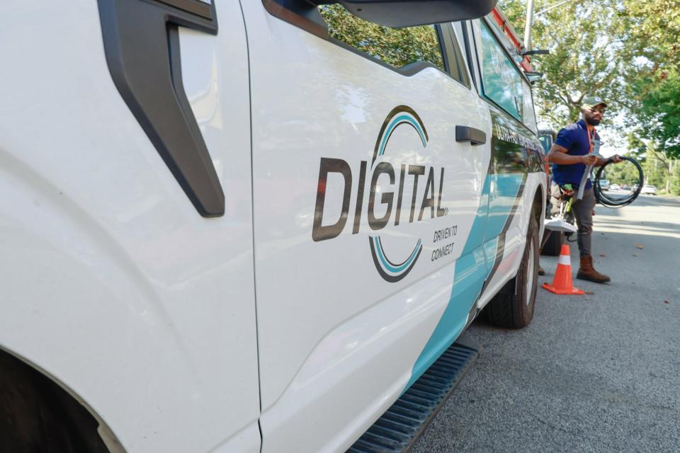 DigitalC service van parked on side of street with worker holding a wire walking behind van