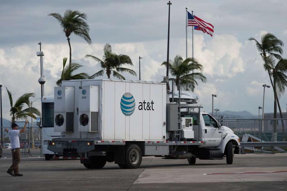 An AT&T truck is parked on a street with an American flag and palm trees in background