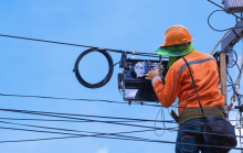 A lineman in an orange shirt works at the top of utility inside fiber splice case