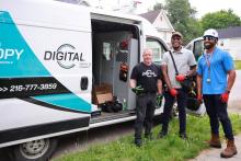 Three DigitalC workers stand outside their parked work van smiling