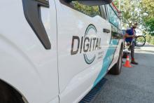 DigitalC service van parked on side of street with worker holding a wire walking behind van